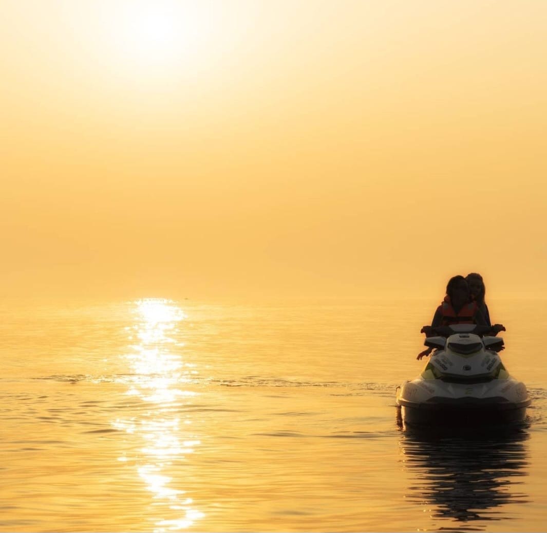 Moto de agua navegando por la costa de Gijón al atardecer con el cielo naranja sobre el Cantábrico.